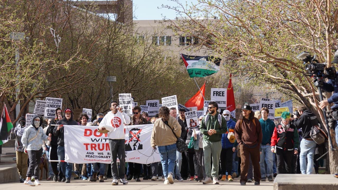 A crowd of people holding banners, signs, and a Palestinean flag.