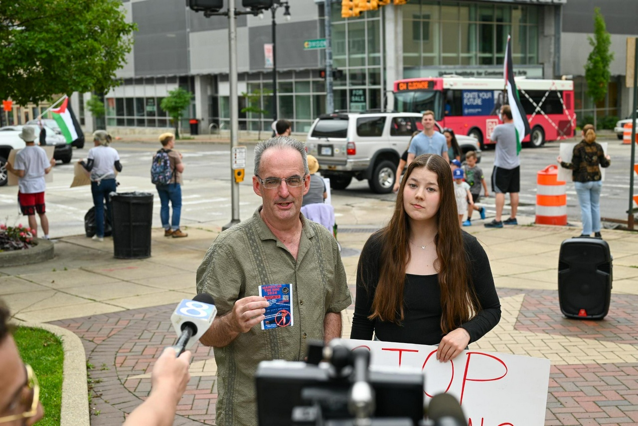 Man and woman give interview to numerous members of the press on a busy streetcorner.