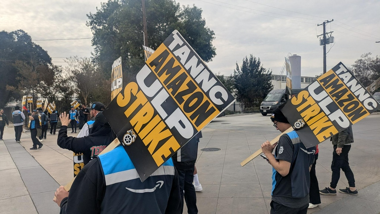 Amazon workers wearing their uniform vests march in a picket line carrying signs supporting the Amazon strike.