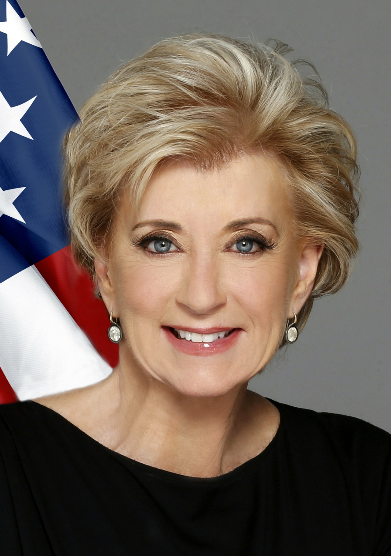 A blonde woman with short hair smiling in front of an American flag.