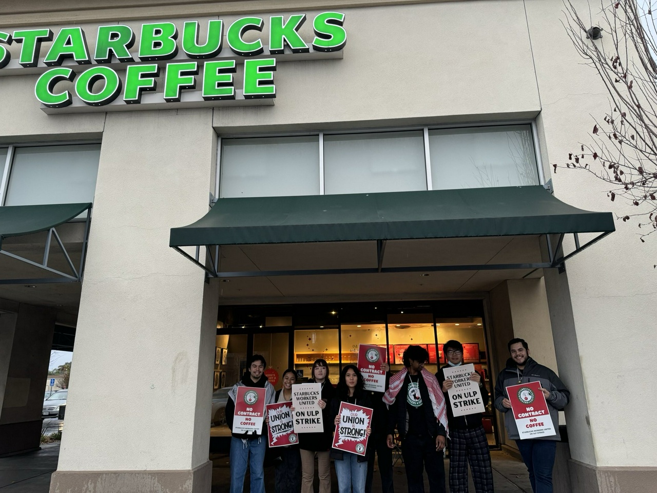 Striking Starbucks workers standing in front of their workplace.