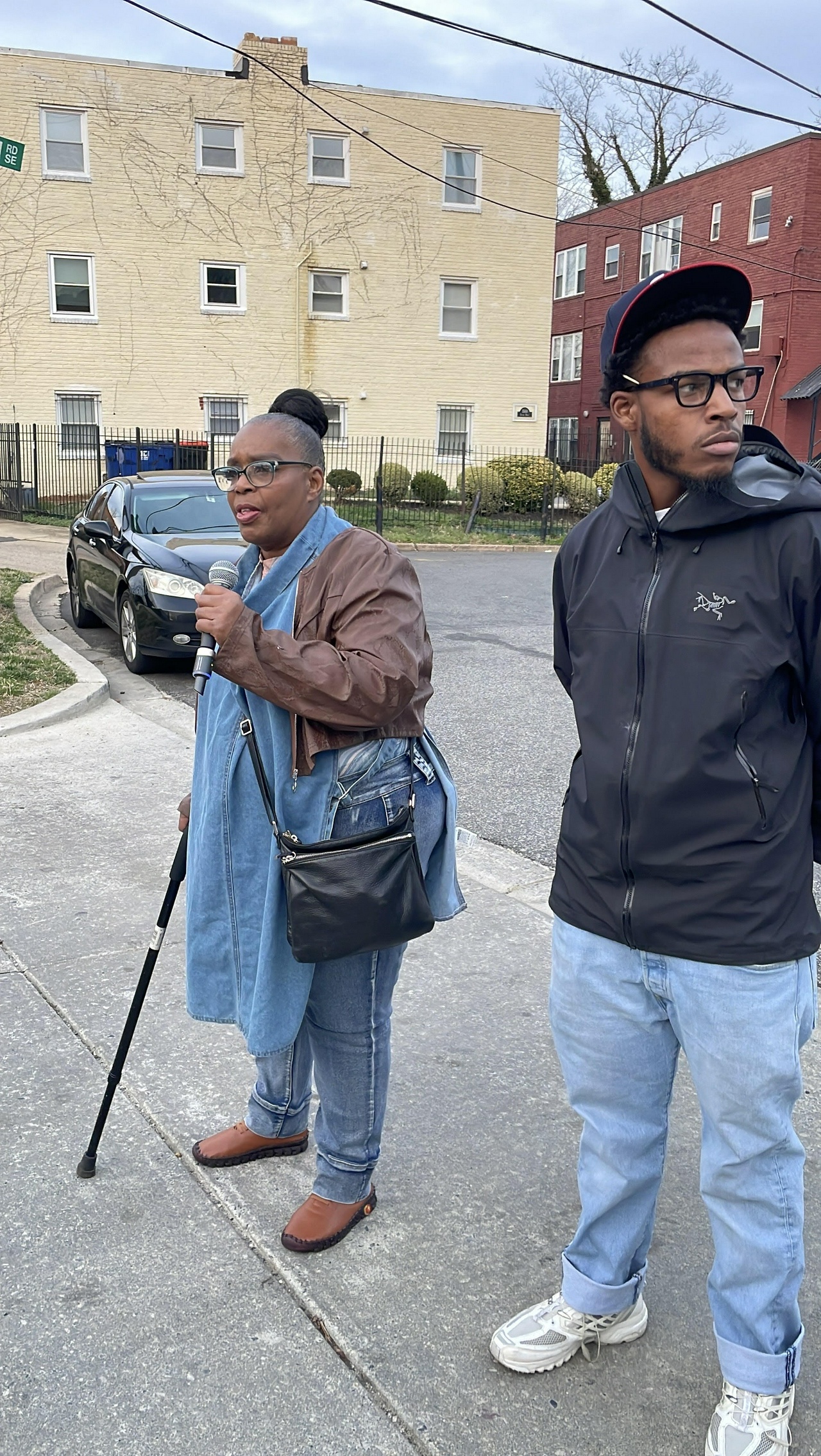 Two members of the Butler family - a middle-aged woman with a cane and a young man - speak to a crowd.