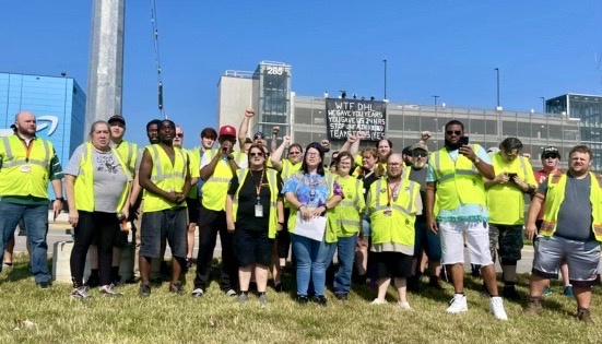 Workers stand with raised fists in front of banner that reads "WTF DHL. We gave you years. You gave us 24 hours. Stop unfair firings. Teamsters yes!”