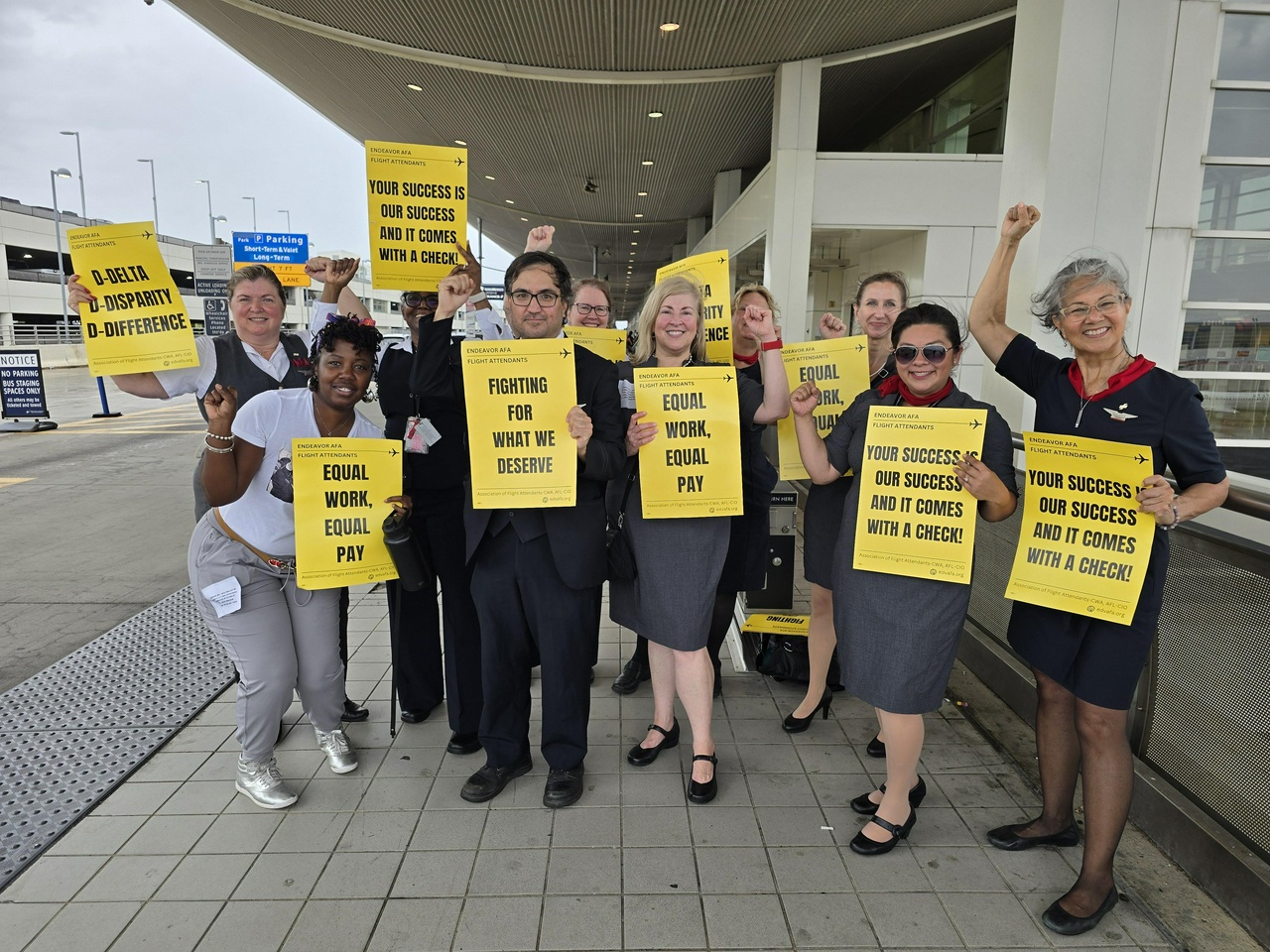 About a dozen workers pose with signs that say slogans like "Equal Work Equal Pay" and "Your success is our success and it comes with a check!"