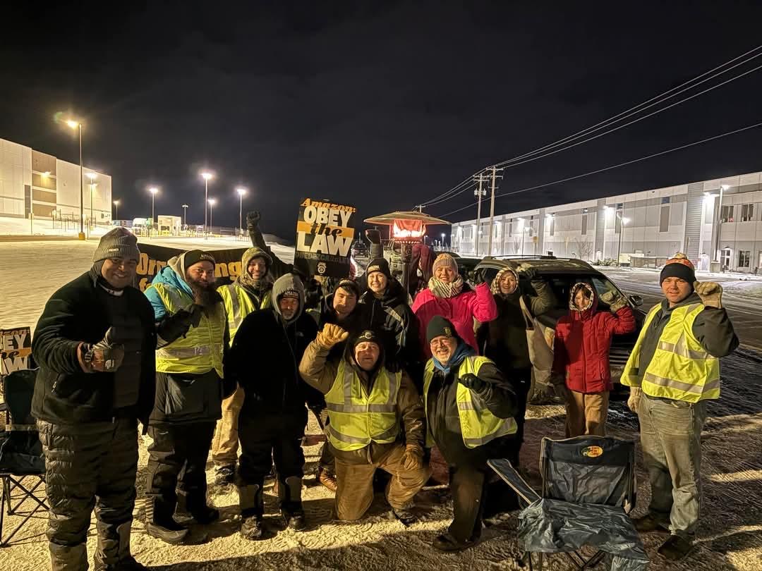 Amazon workers and supporters pose with raised fists near a snow covered roadway.