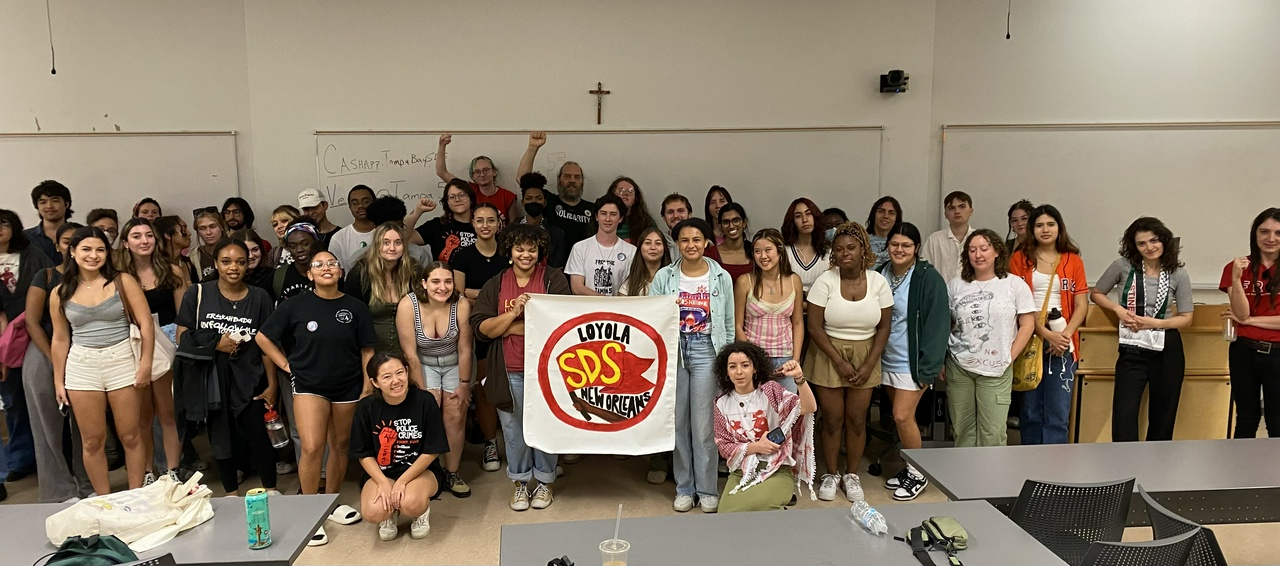 Speaking event participants pose behind Loyola SDS banner. | Fight Back! News/staff