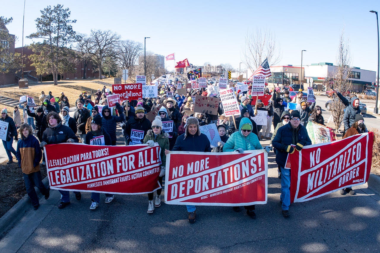 Protesters march behind banners that read “Legalizacion para todxs, Legalization for All, Minnesota Immigrant Rights Action Committee,” “No more deportations, MIRAC-Minnesota Immigrant Rights Action Committee,” and “No Militarized Border, MIRAC.”