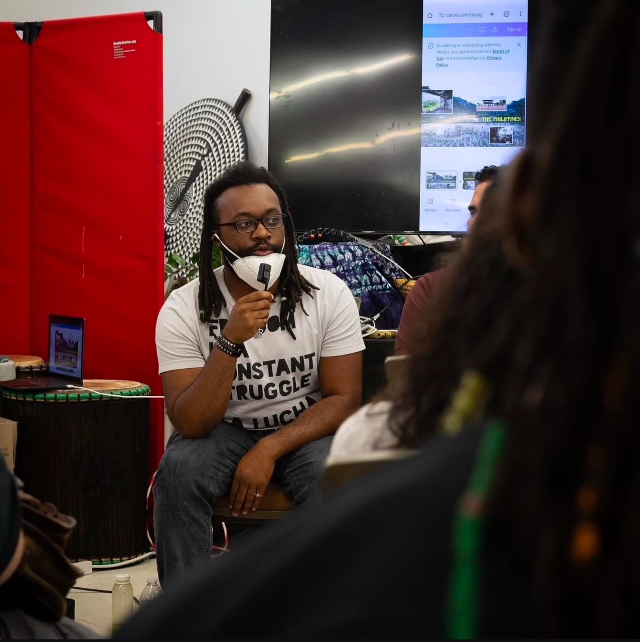 A man with glasses sits speaking with a group of people.