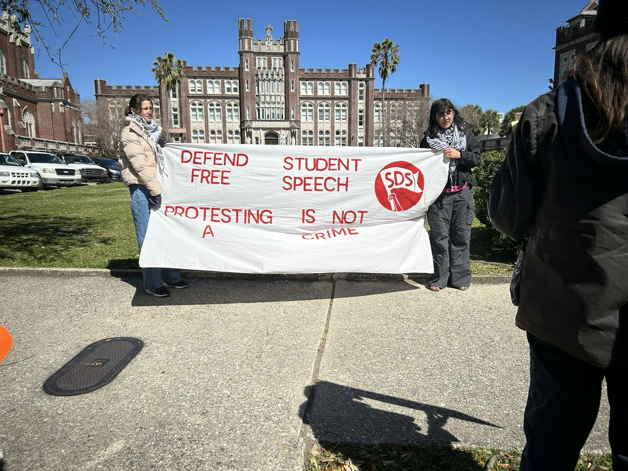 Students hold a banner in front of Loyola University that reads "Defend student free speech, Protesting is not a crime."