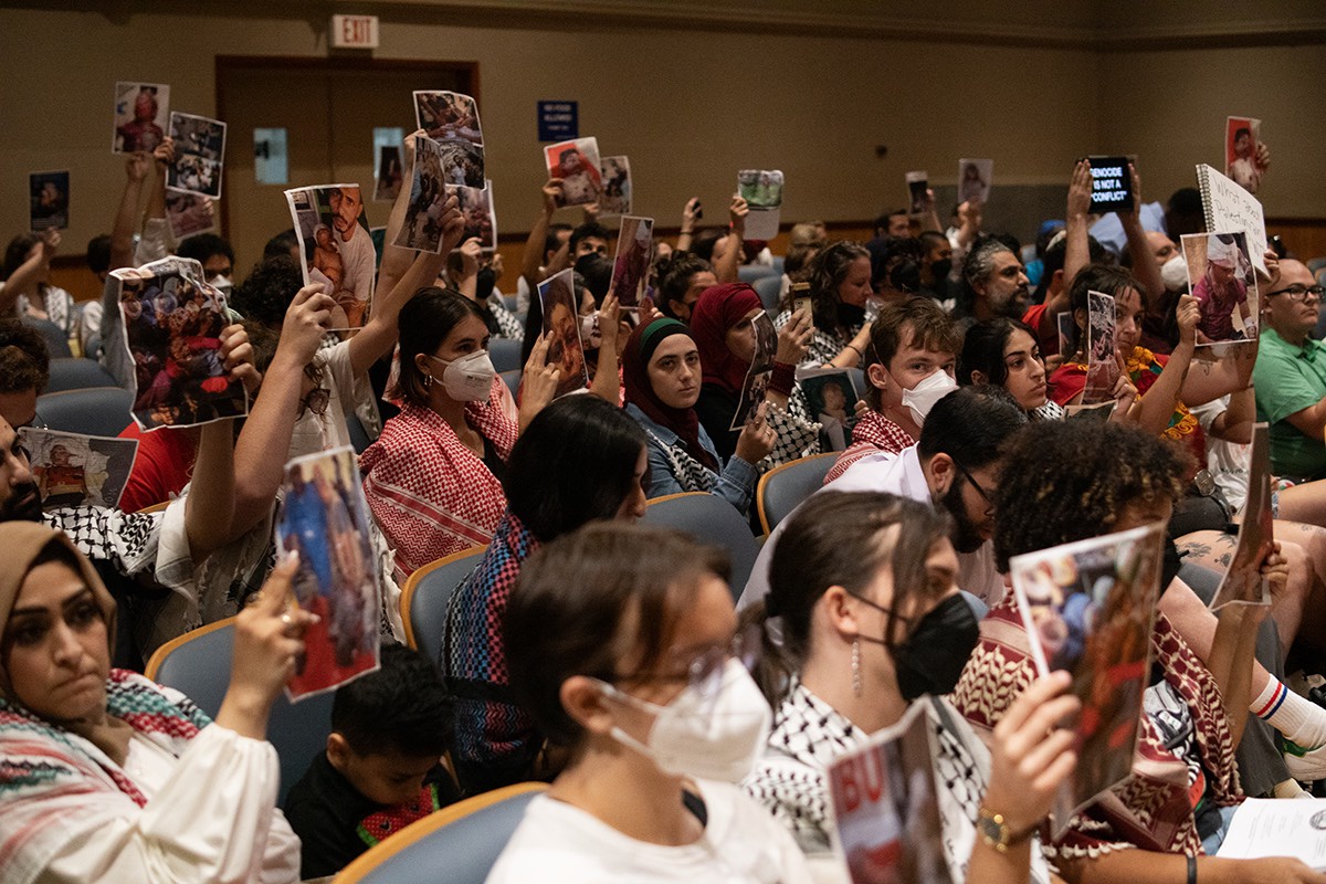 Protesters at city hall hold up pictures of Israeli atrocities.