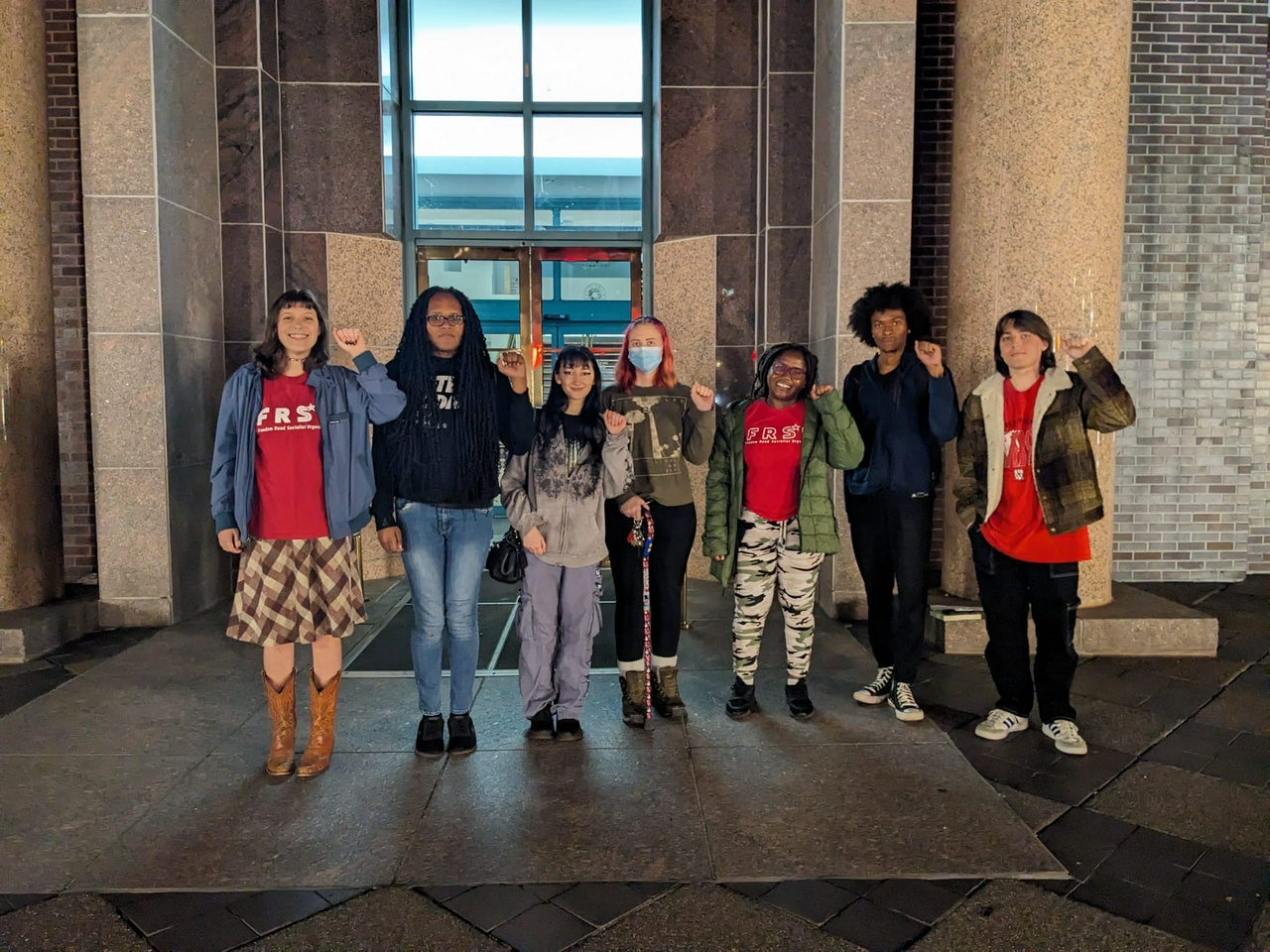 Activists hold up their fists in front of a government building.