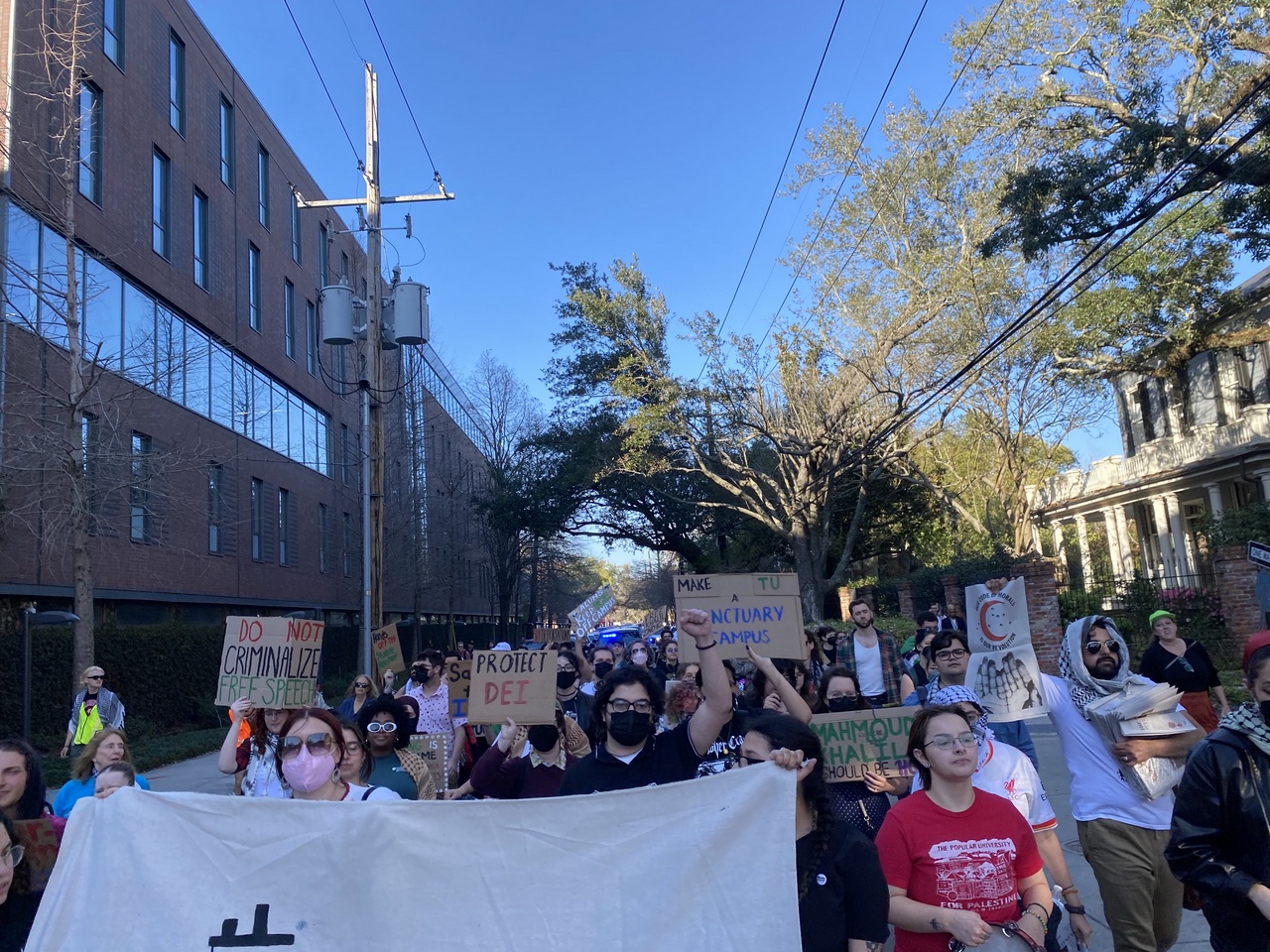 Protesters march in the street carrying signs with slogans like “ Do not criminalize free speech”.