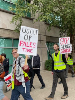 Marchers walk holding signs that read "US out of Palestine" and "Stop aiding genocide."