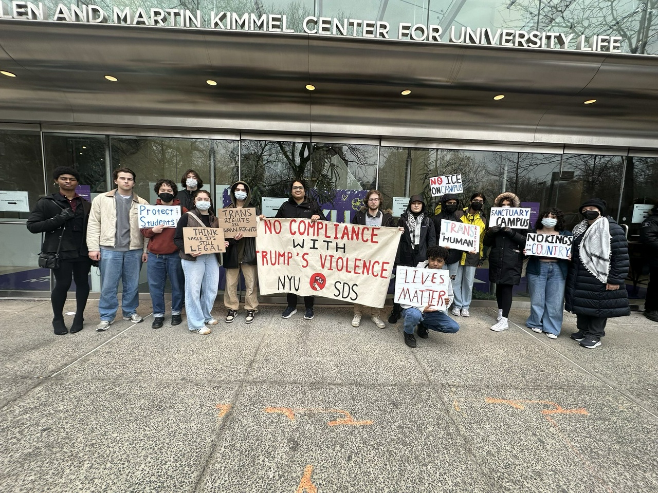 Students gather in front of Kimmel Center for University Life with signs and banners reading slogans including, “Sanctuary campus,” “Think while it’s still legal,” and “No compliance with Trump’s violence. NYU SDS”