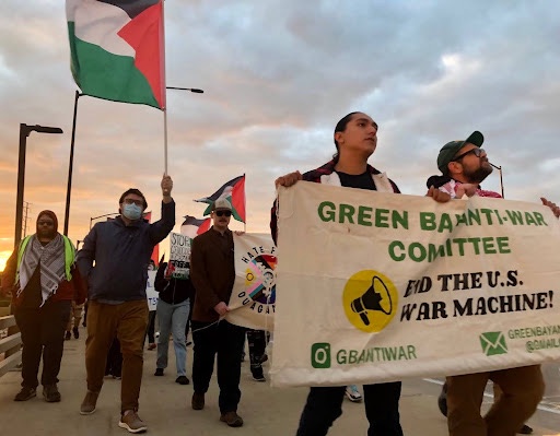 Protestors hold Palestinian flags and march behind a banner that reads “End the US War Machine”.