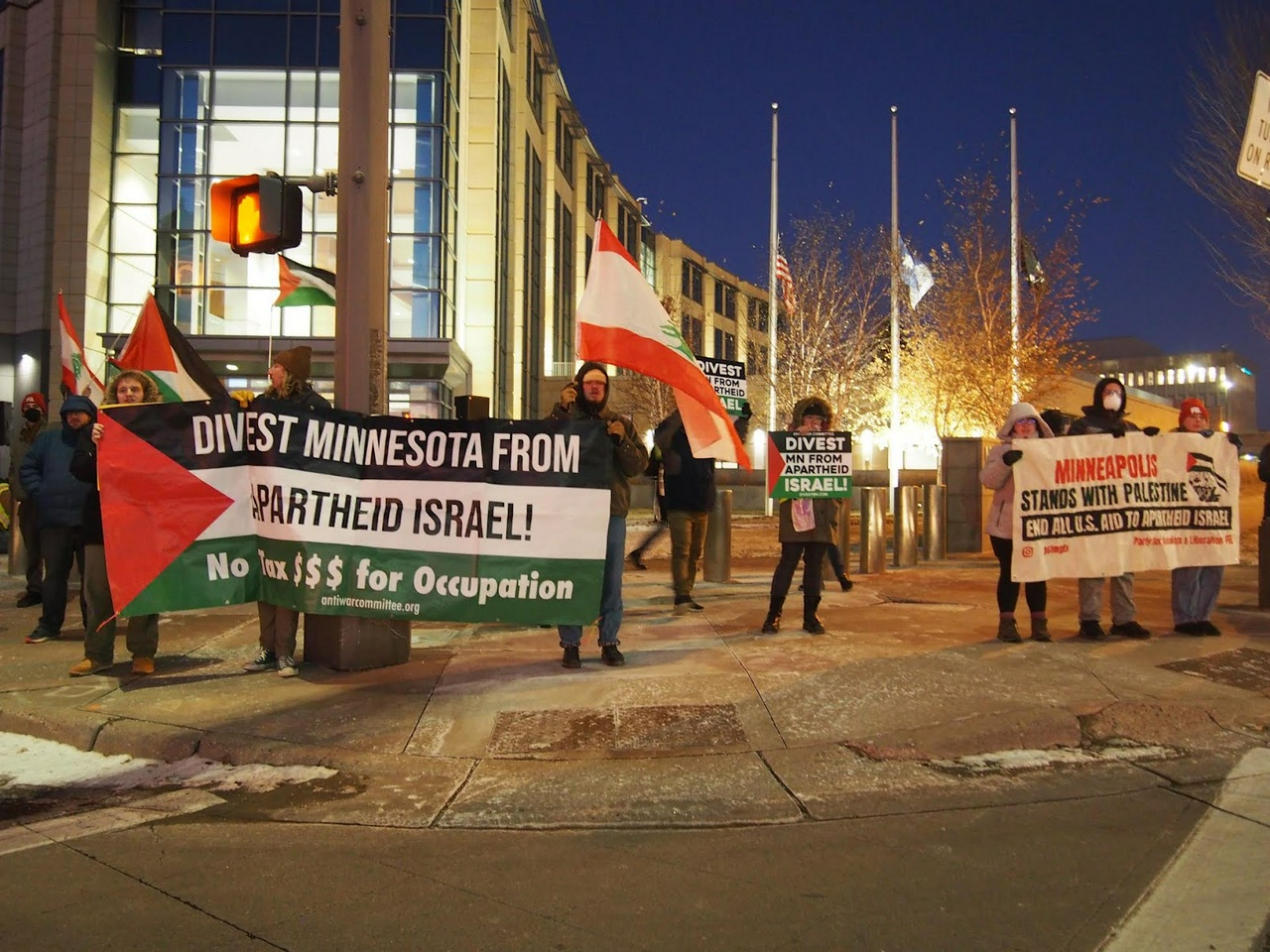 People holding pro-palestine banners and flags on a sidewalk.