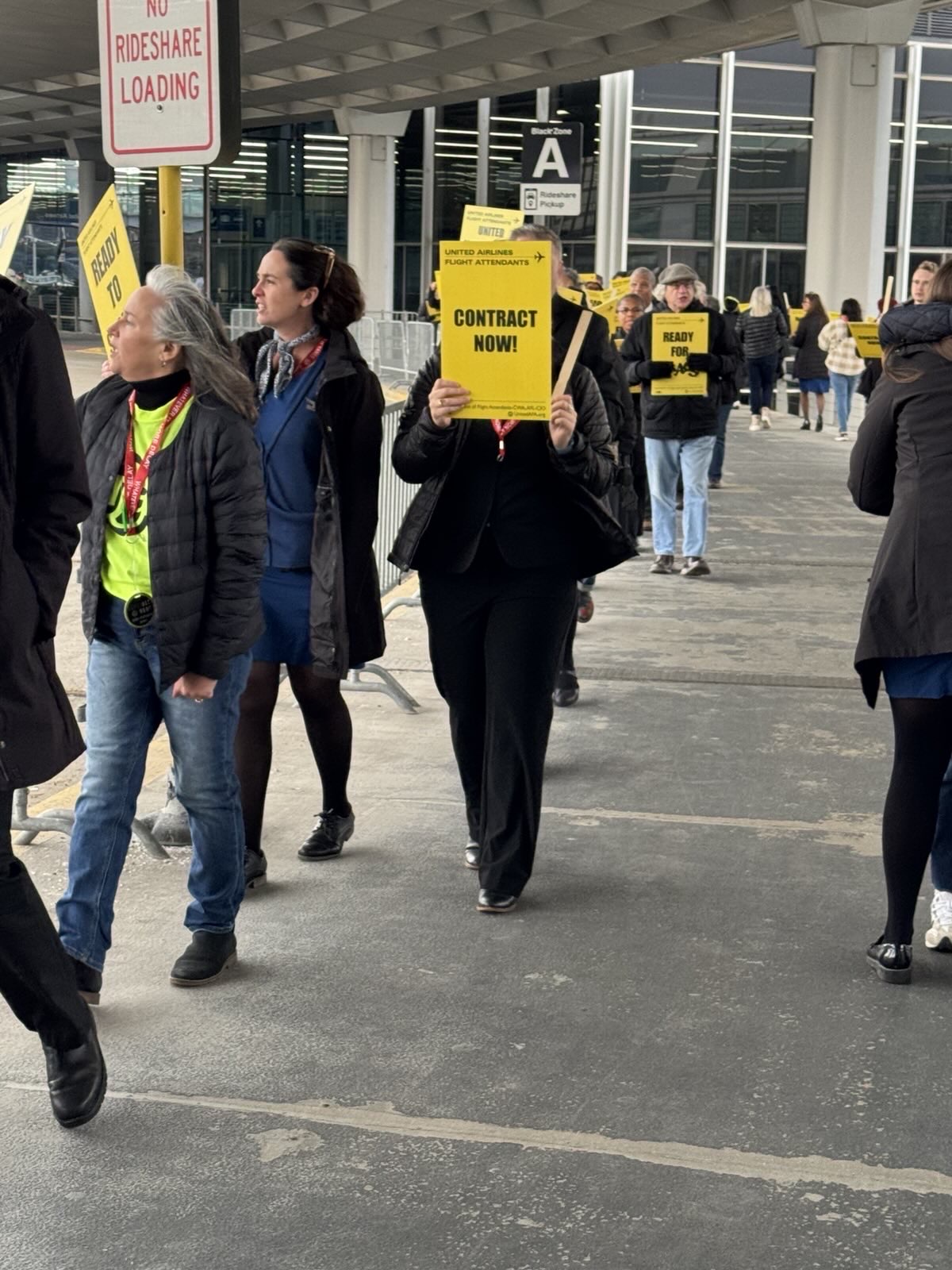 A crowd of people walking holding signs reading, "Contract Now!"