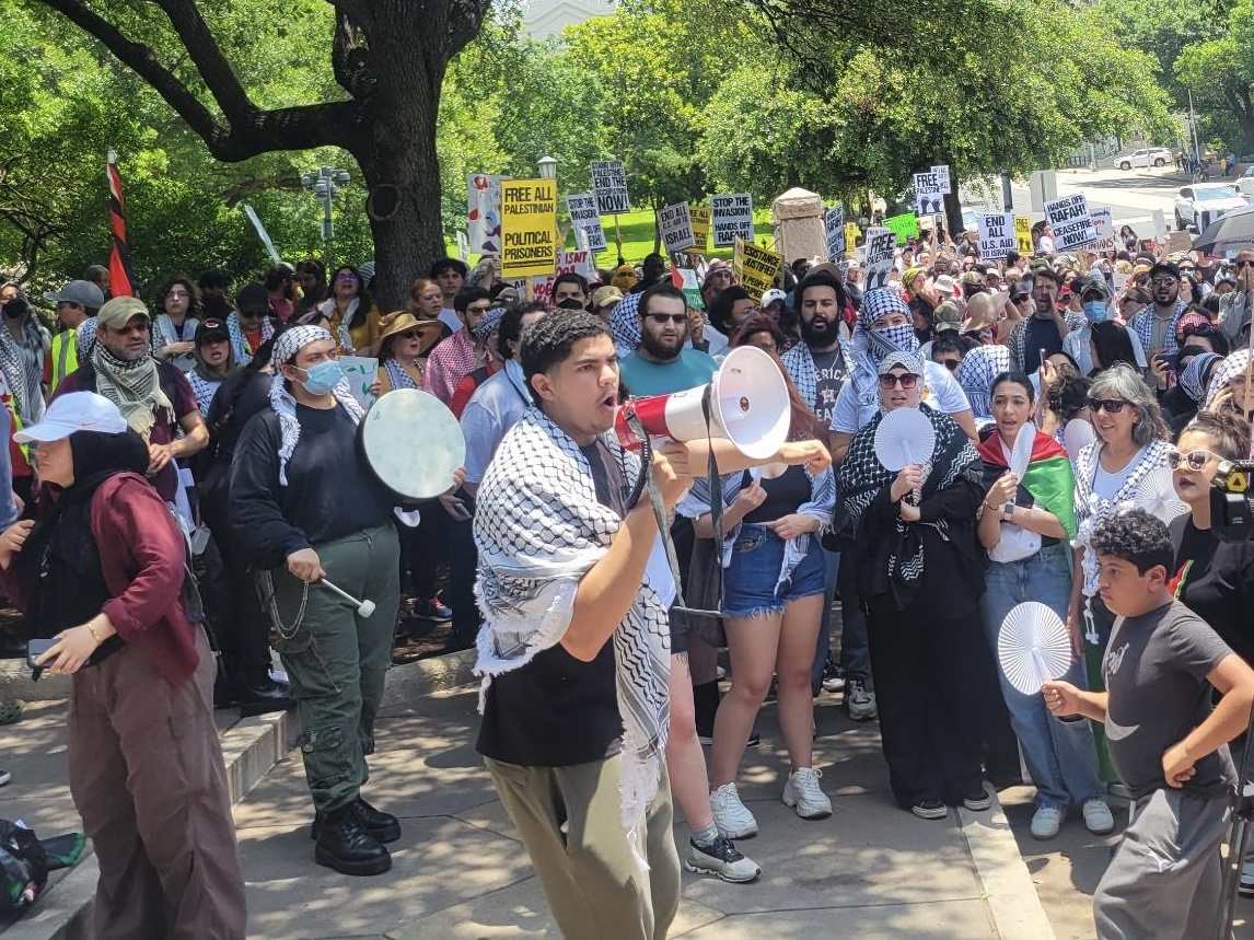 Activist wearing keffiyeh holding megaphone surrounded by over a hundred onlookers