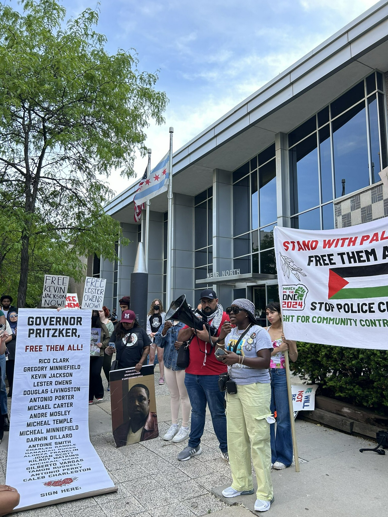 Protestors hold signs saying “Free Them All” while a woman speaks over a bullhorn.