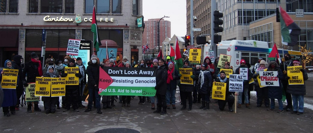 A pro-Palestine protest outside of a Caribou coffee with people holding signs.