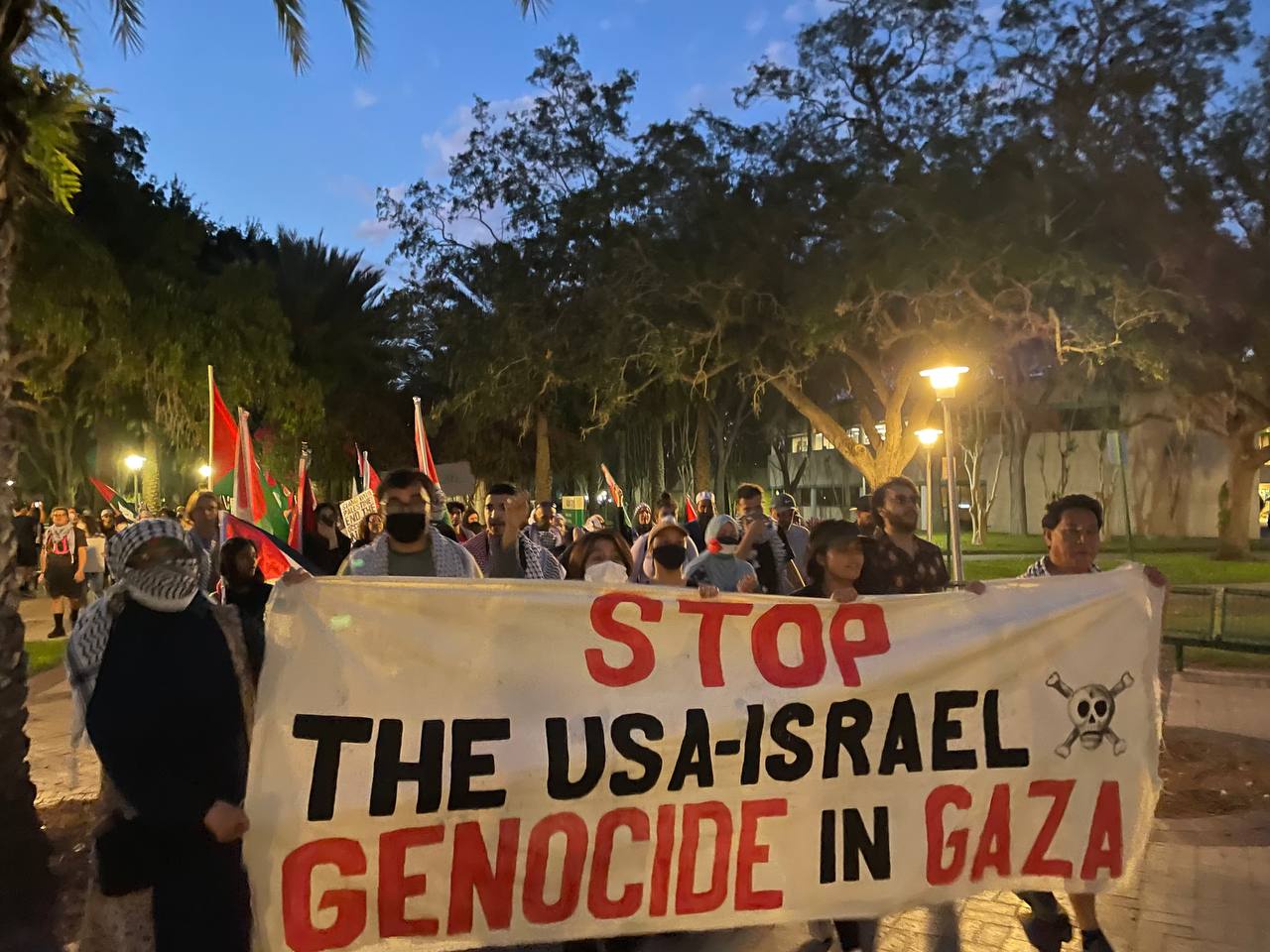 Crowd marches carrying Palestinian flags lead by a group carrying a banner that reads "STOP THE USA-ISRAEL GENOCIDE IN GAZA"