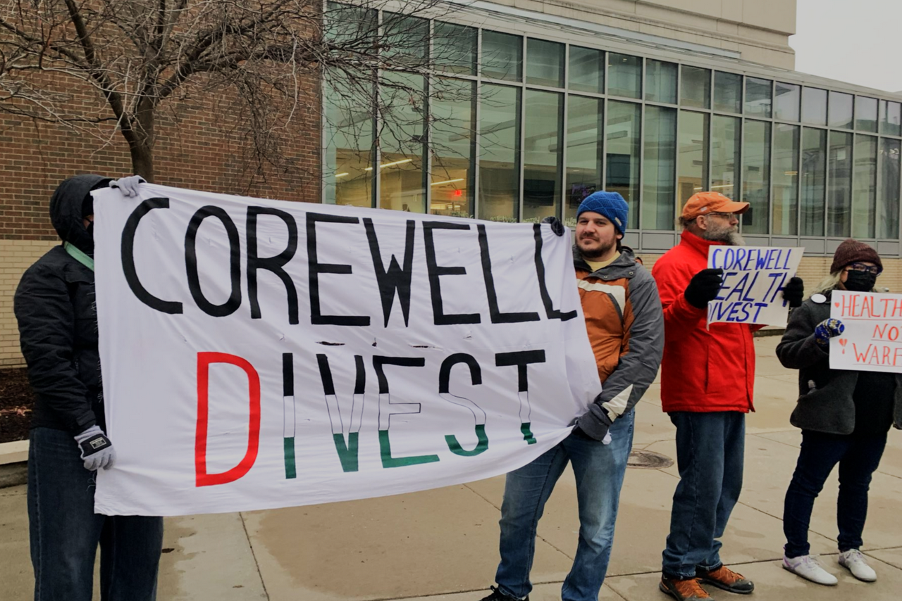 A group of protesters hold signs outside of Corewell Health calling for divestment from Israel