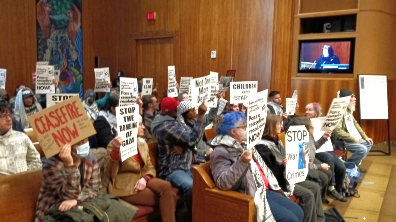Activists, many wearing keffiyehs, hold signs that read "Stop war crimes," "Ceasefire now," and more.